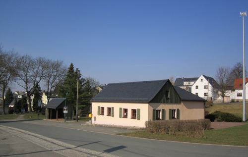 Auf dem Bild stellt sich das Dorfhaus aus Richtung Mechelgrün kommend dar. Es hat eine gelbliche Fassade und ein grünes Dach. Das Dorfhaus befindet sich im Ortskern von Zobes.